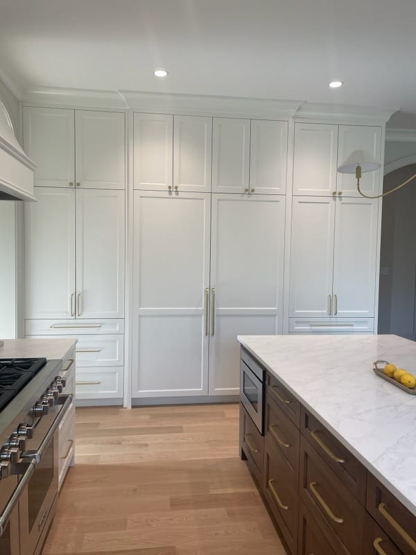 Two-tone kitchen with full-height white cabinetry and a dark wood island topped with white stone