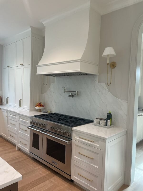 White custom kitchen cabinetry surrounding a professional range and sculpted range hood