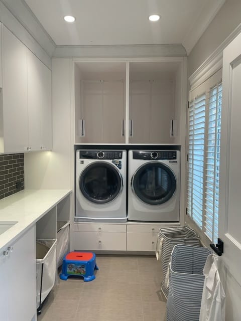 Light painted laundry room cabinetry built around a washer and dryer with drawers, upper cabinets, side counters, and open cubbies