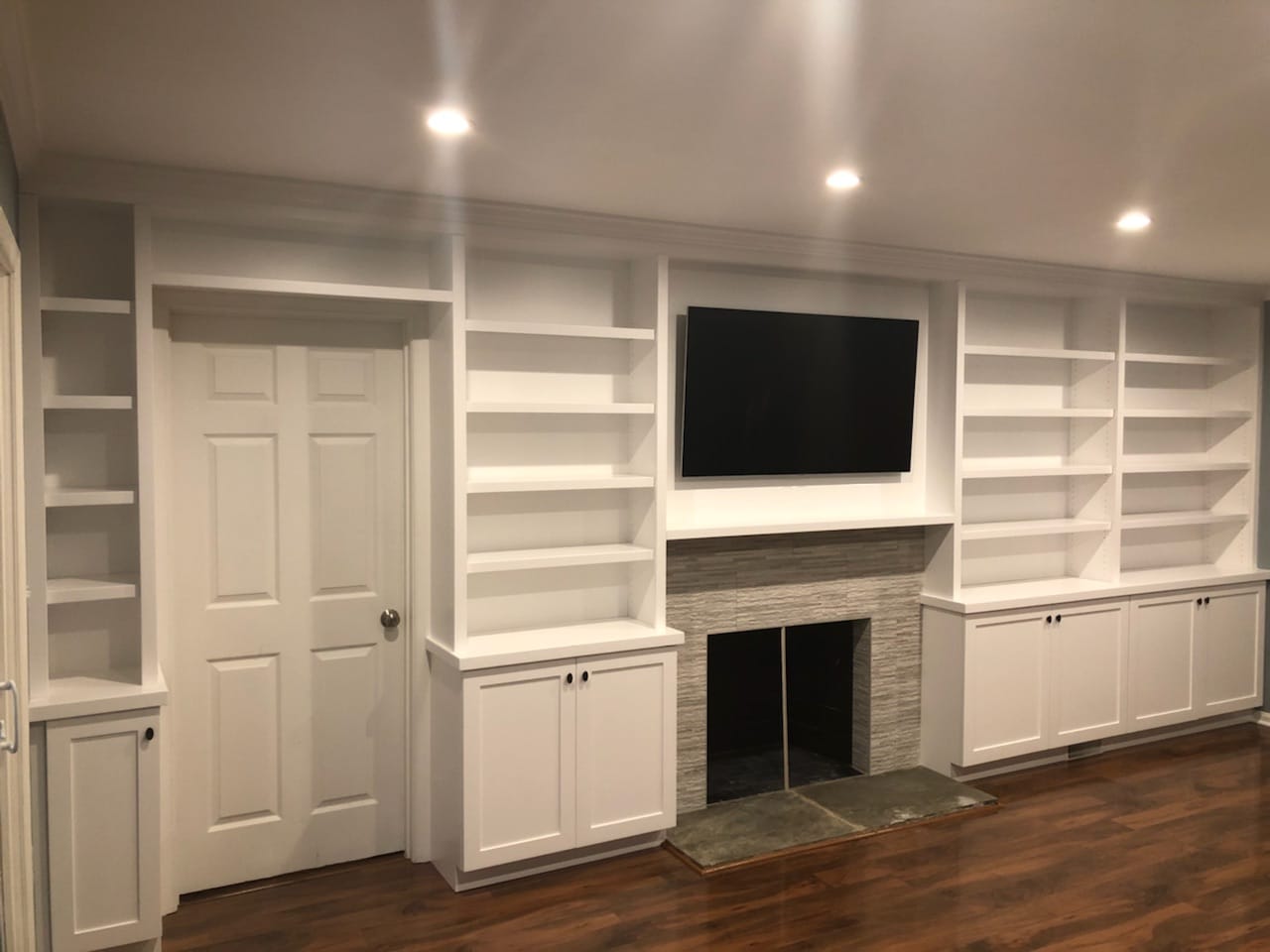 White built-in media wall with open shelves, lower cabinet doors, television, fireplace, and cabinetry around a doorway