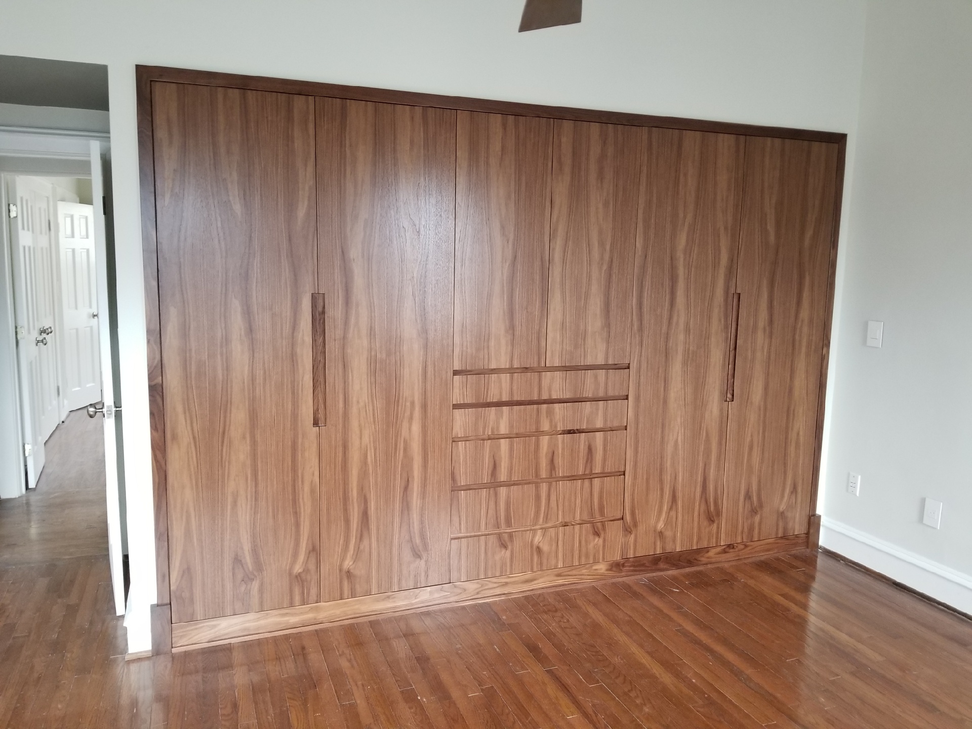 Custom wall-to-wall walnut wardrobe with integrated drawers and recessed handles